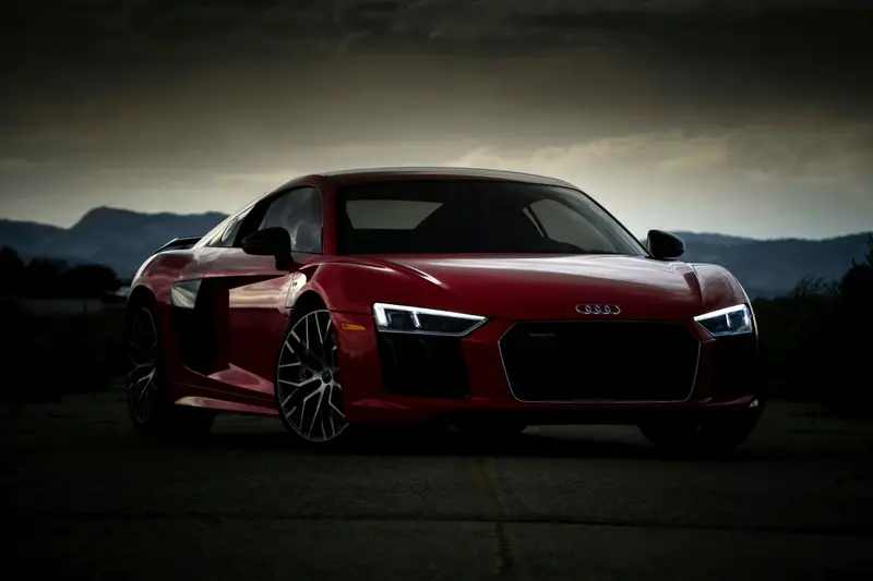 Red Audi R8 with its headlights on, parked on an open road at dusk with mountains behind