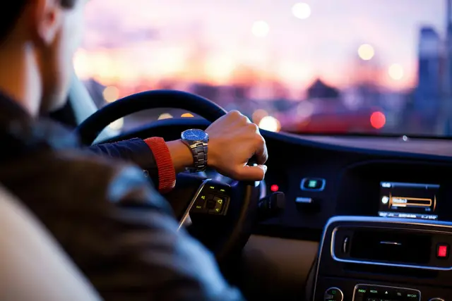 Driver's hands on a steering wheel at dusk